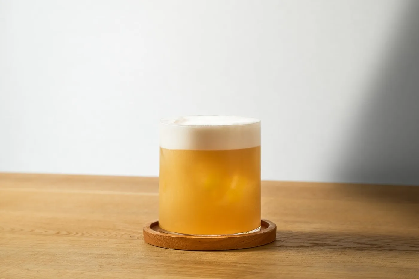 L'Amaretto Sour servito in un tumbler basso con la sua schiuma compatta in superficie, su un sottobicchiere in legno