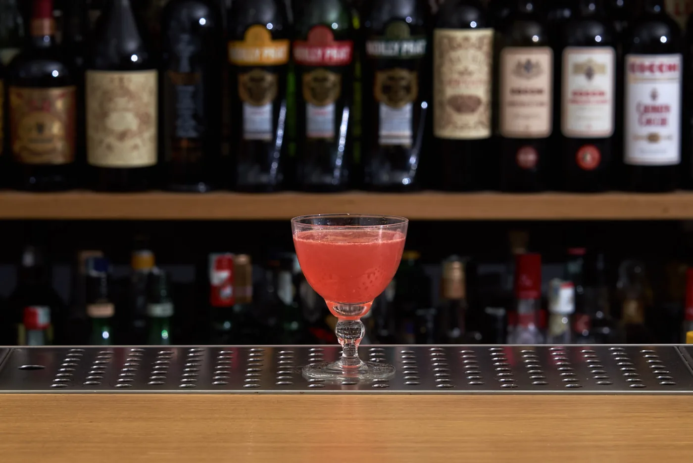 Bacardi Cocktail rosa in coppetta su banco bar, con bottiglie di vermouth sullo sfondo