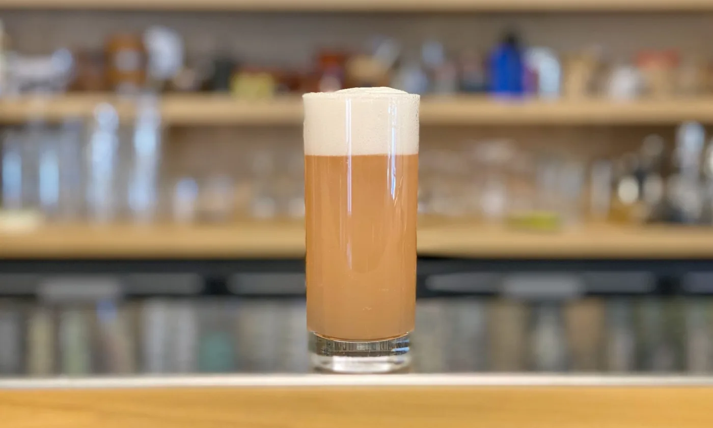 Bellini Scientifico: tumbler alto con drink rosato e schiuma bianca compatta sul banco di lavoro