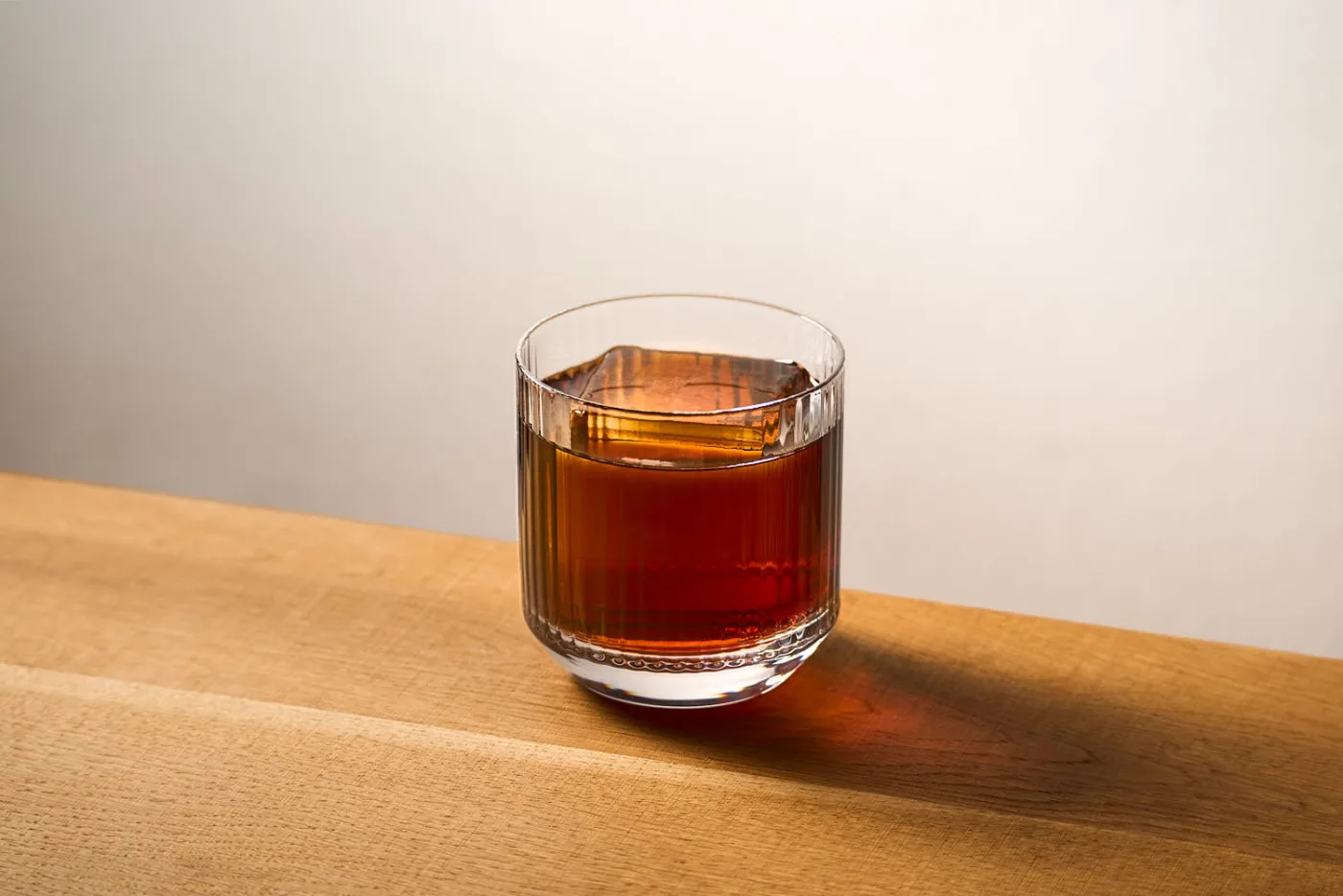 Il Black Russian servito in un tumbler basso rigato con un chunk di ghiaccio, su un tavolo in legno