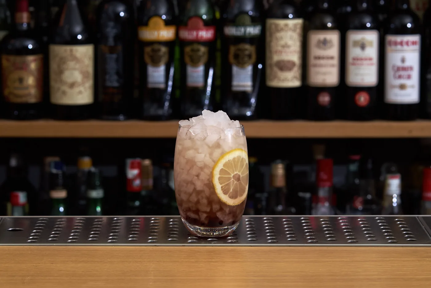Bramble con ghiaccio tritato, crème de mûre sul fondo e ruota di limone su banco bar