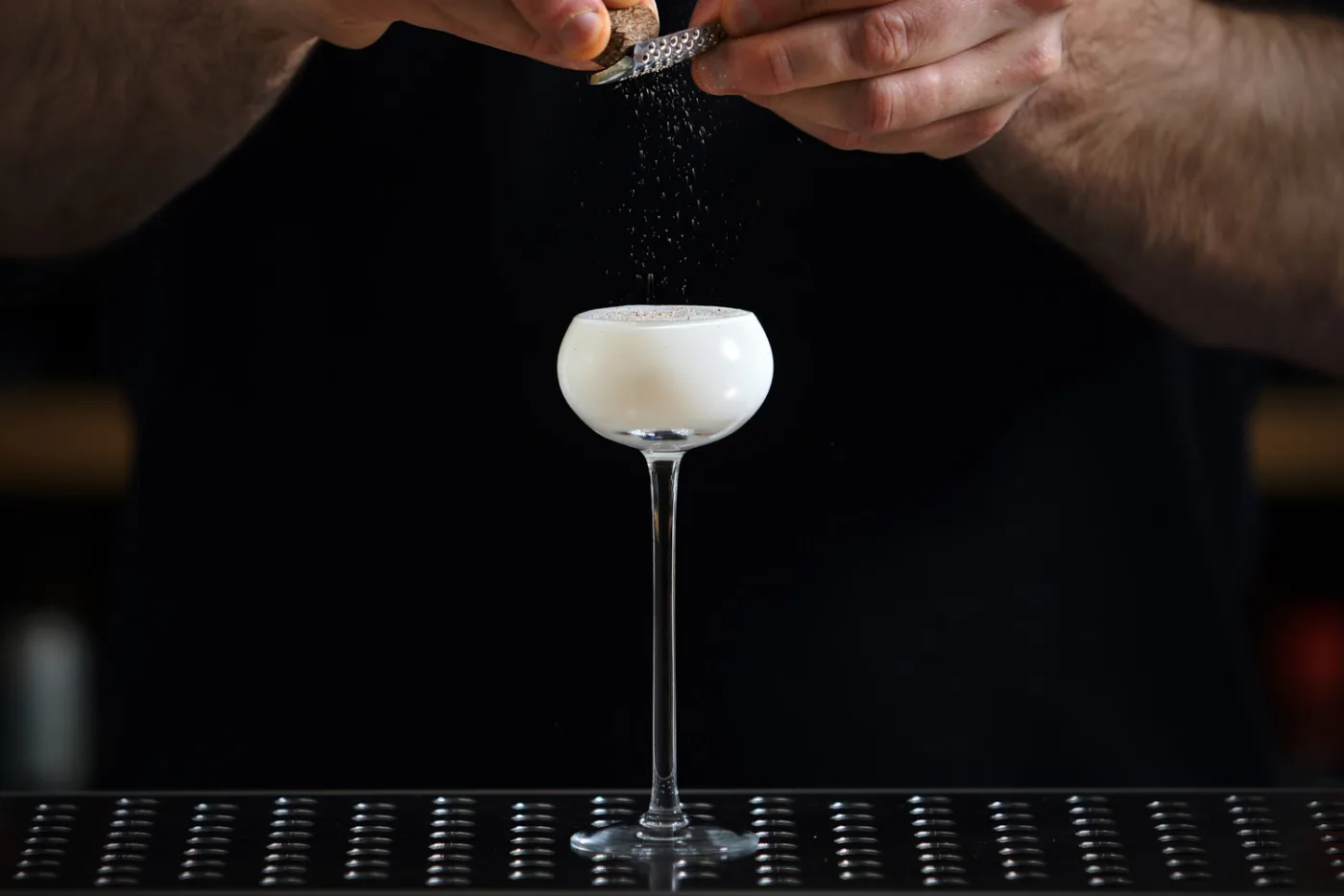 Bartender grattugia noce moscata su un Brandy Alexander bianco in coppa a stelo lungo