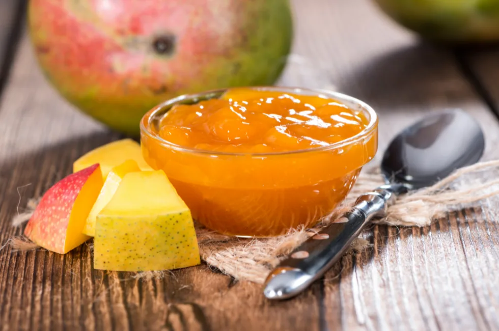 Ciotolina di chutney al mango con cucchiaio e pezzi di mango fresco