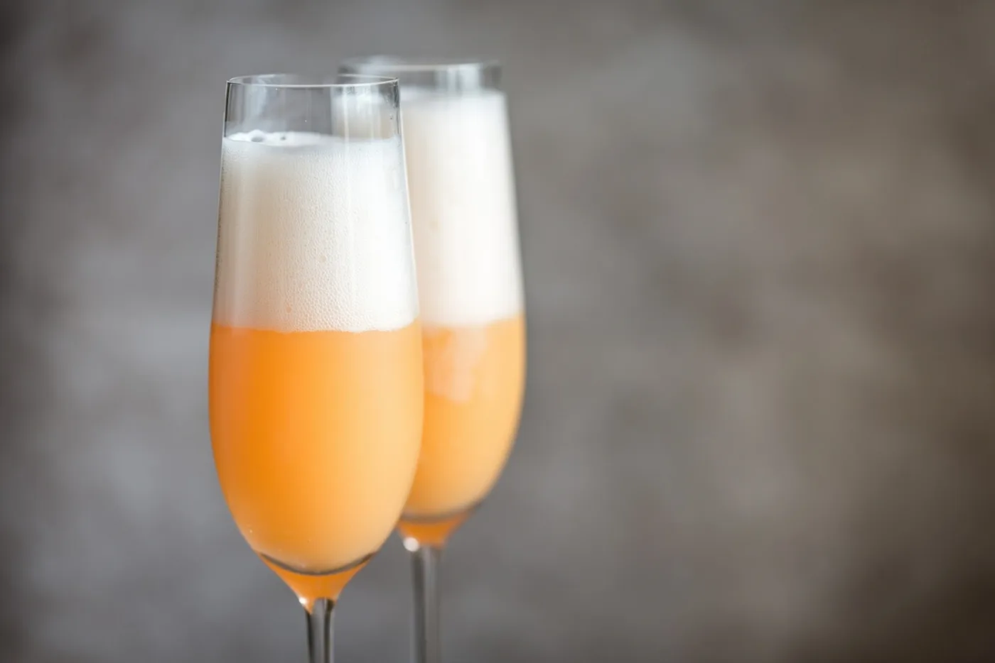 Due Bellini bianco-rosati in flûte con schiuma abbondante in superficie