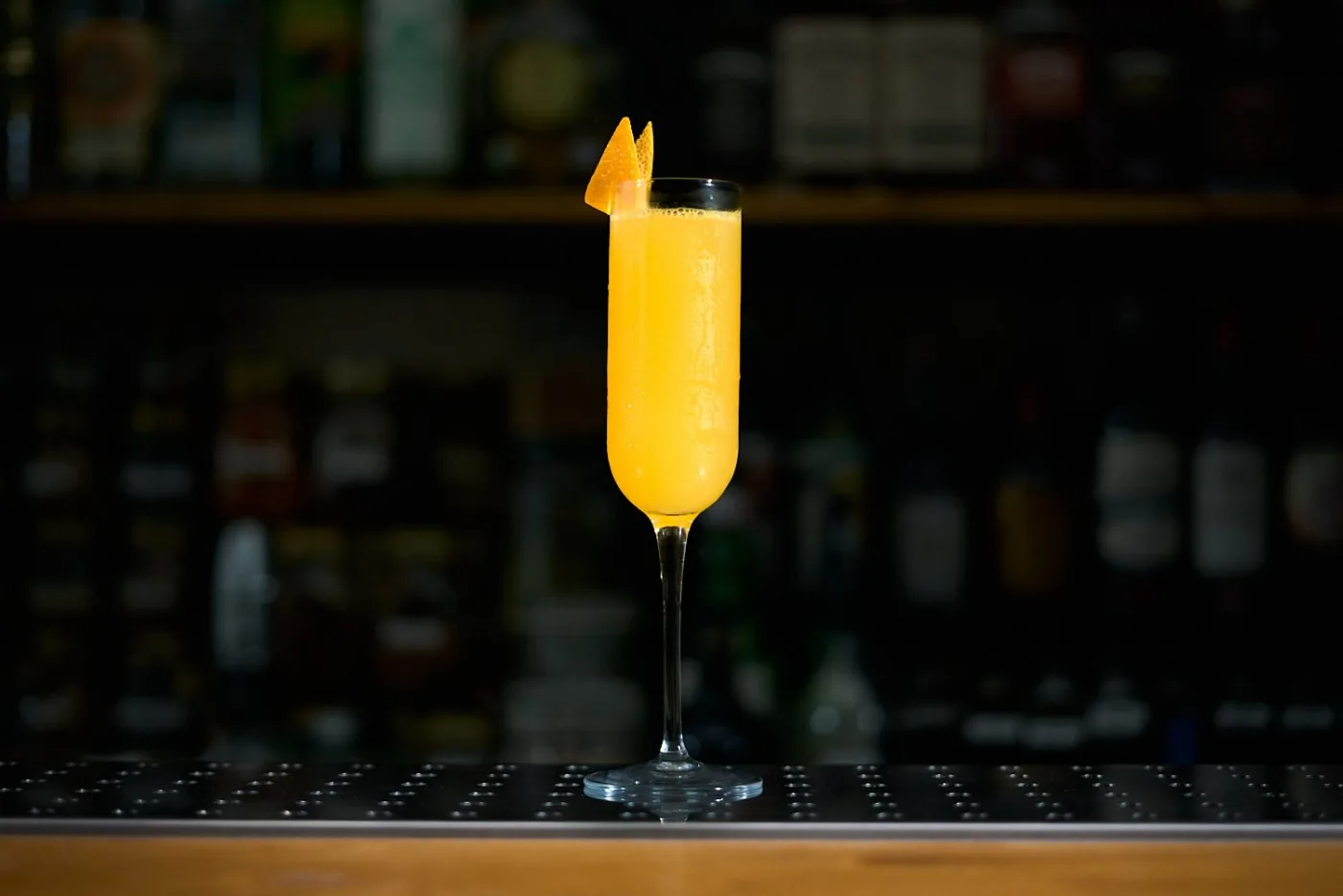 Il cocktail Mimosa servito in un flute alto e stretto, decorato con una scorza d'arancia, su un banco bar