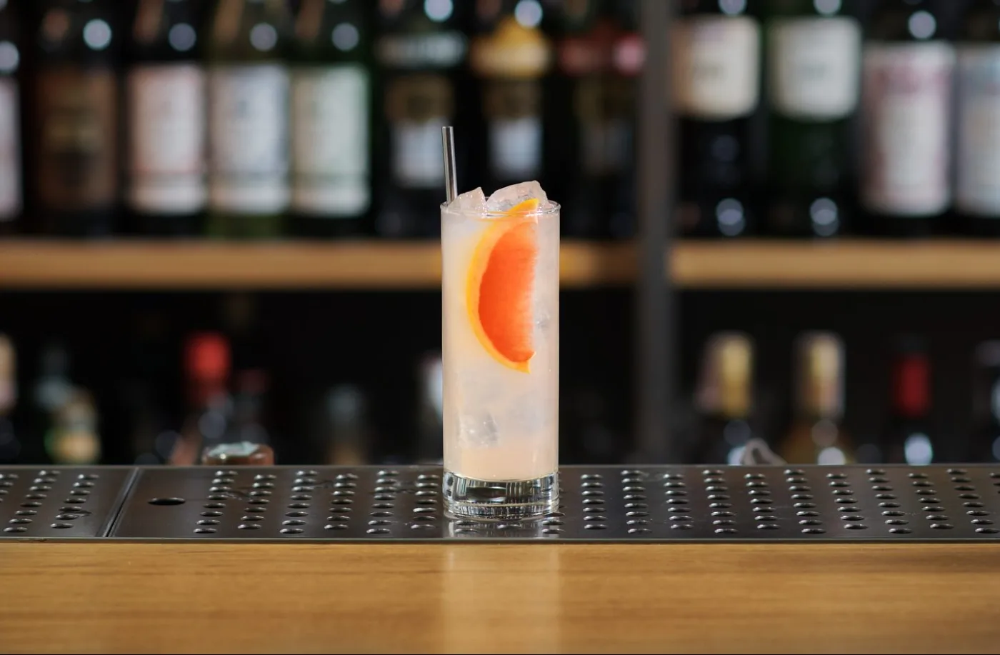 Paloma in tumbler alto con ghiaccio, cannuccia e spicchio di pompelmo rosa su banco bar