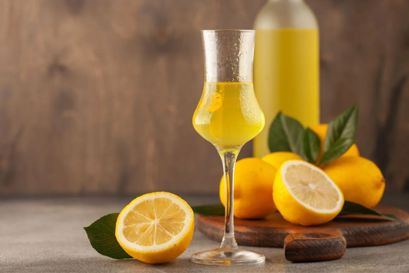 Bicchierino di limoncello con limoni freschi e bottiglia su fondo di legno