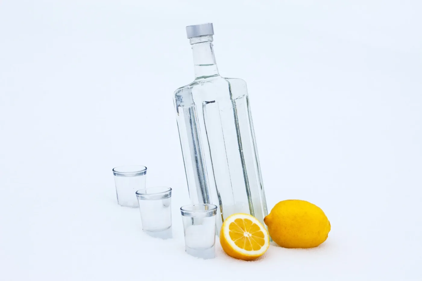 Bottiglia di vodka nella neve con un limone intero, mezzo limone e tre bicchierini
