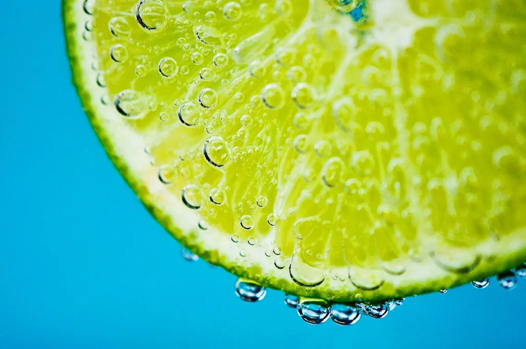 Fetta di lime immersa in acqua frizzante con bollicine su fondo azzurro