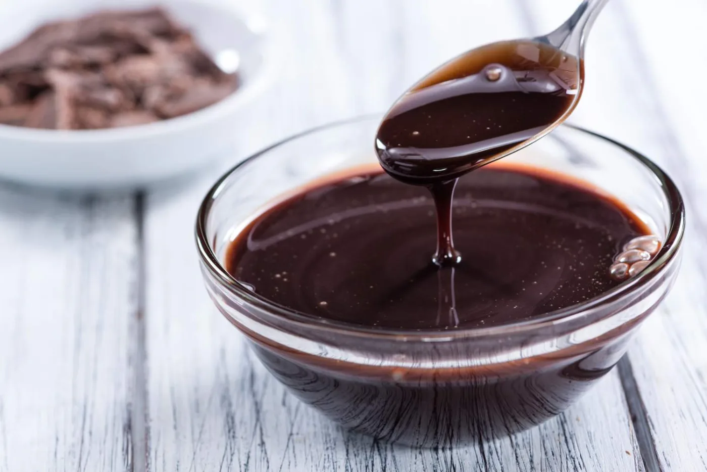 Riduzione scura e sciropposa in una ciotolina di vetro, raccolta con un cucchiaio da cui cola densa