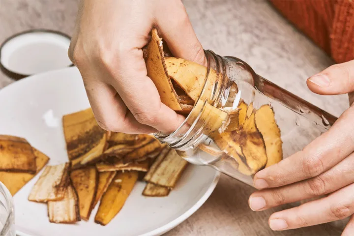 Mani che riempiono un barattolo di vetro con bucce di banana tagliate