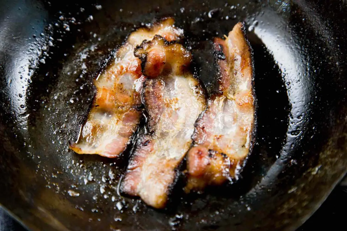 Fette di bacon che rilasciano il loro grasso cuocendo in una padella di ferro