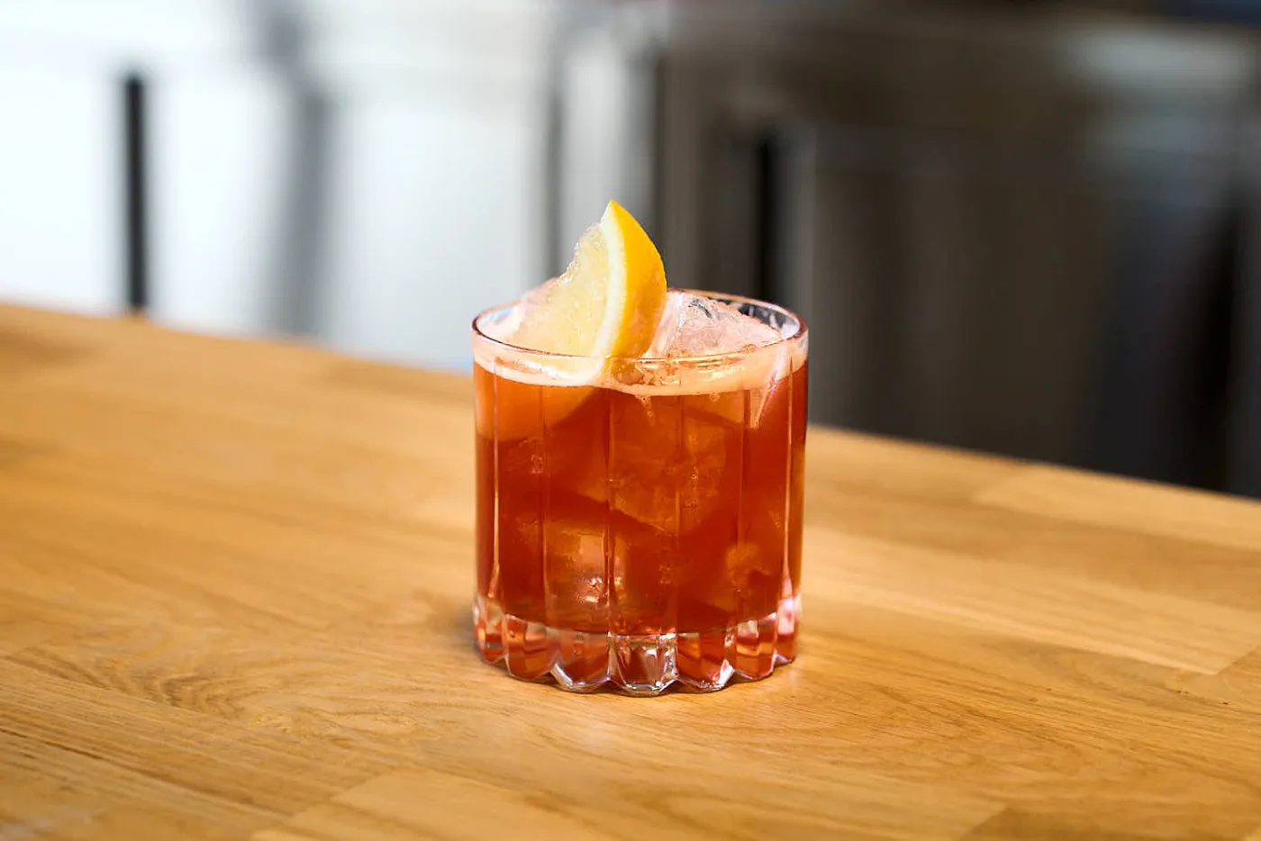 Cocktail Fellini rosso in tumbler basso sfaccettato con ghiaccio e spicchio di limone