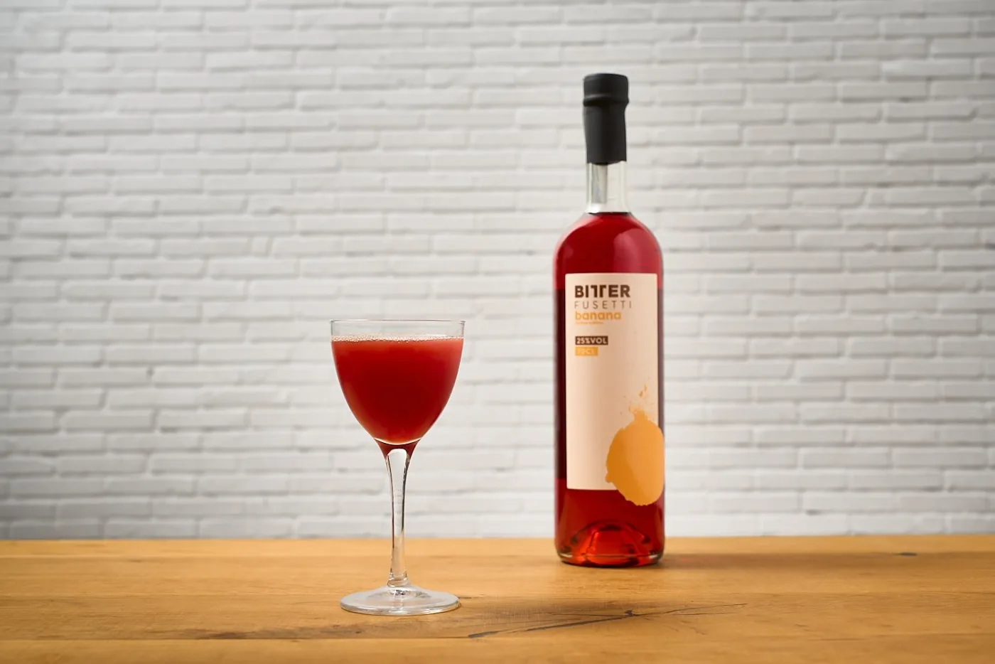 Fusettino: cocktail rosso in coppetta Nick and Nora accanto alla bottiglia di Bitter Fusetti alla banana
