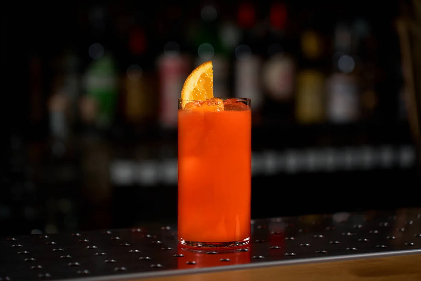 Su un banco bar, un bicchiere da Long drink contenente il cocktail Garibaldi, decorato con una fetta di arancia