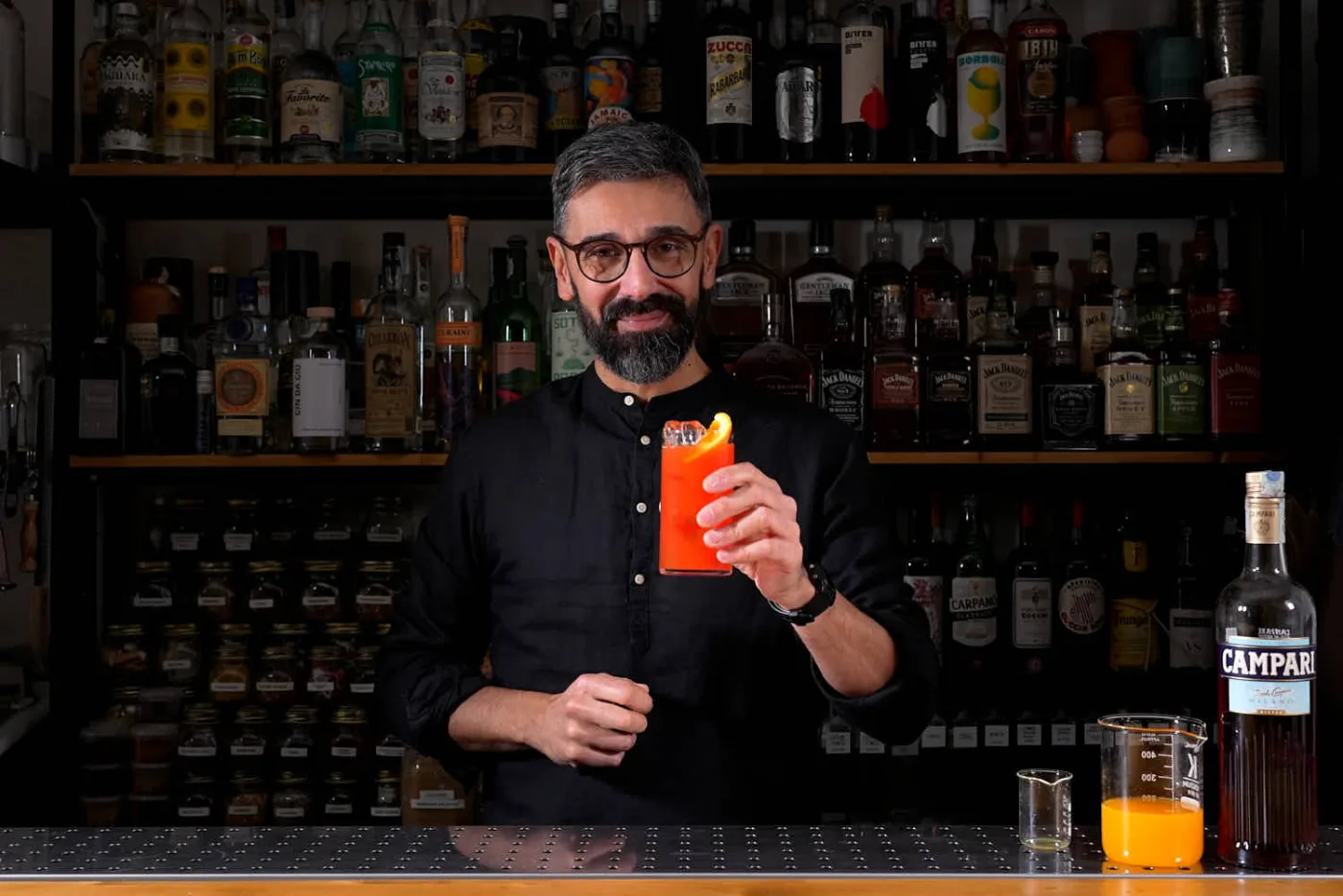 Il bartender dietro al banco mostra un Garibaldi appena preparato, con la bottiglia di Campari e il succo d'arancia accanto