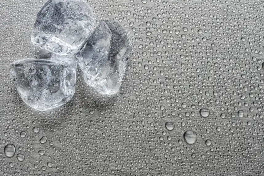 Tre cubetti di ghiaccio su una superficie grigia coperta di gocce di condensa