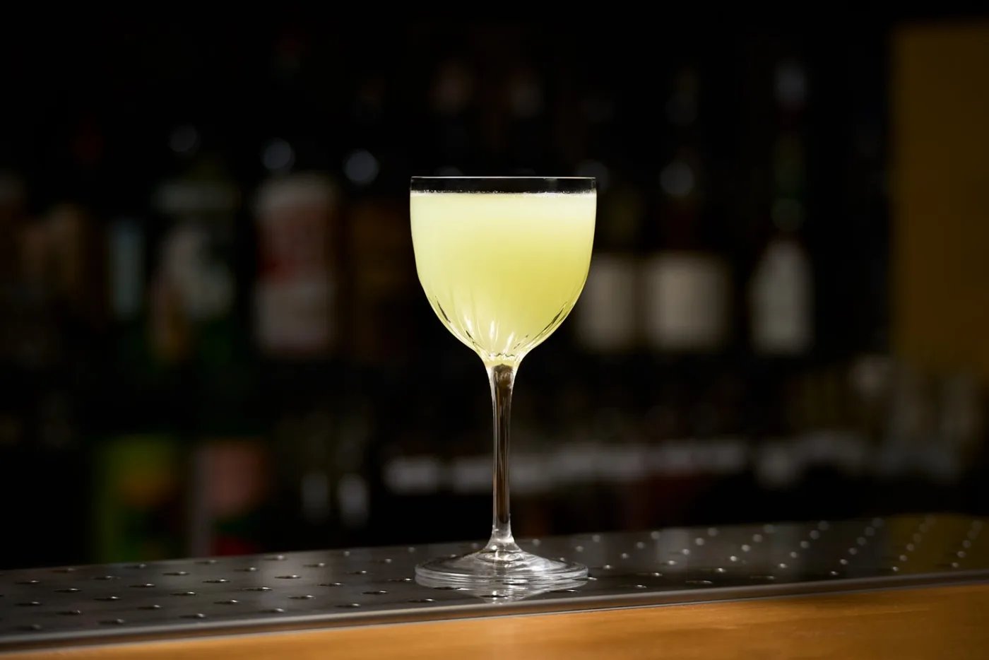 Il Gimlet, dal colore giallo-verde chiaro, servito in una coppetta Nick & Nora su un banco bar