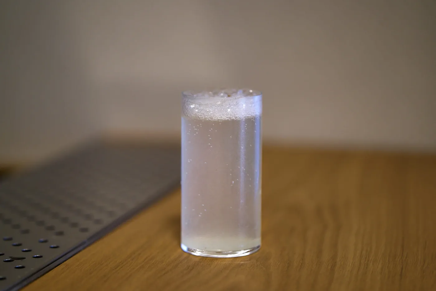 Gin Fizz in tumbler alto senza ghiaccio, con leggera schiuma ed effervescenza, su banco bar in legno