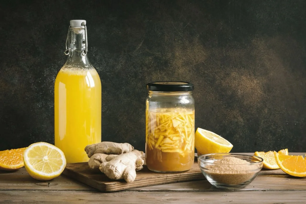 Bottiglia di ginger beer home made con tappo meccanico accanto a un barattolo di zenzero in fermentazione, radice di zenzero e limoni