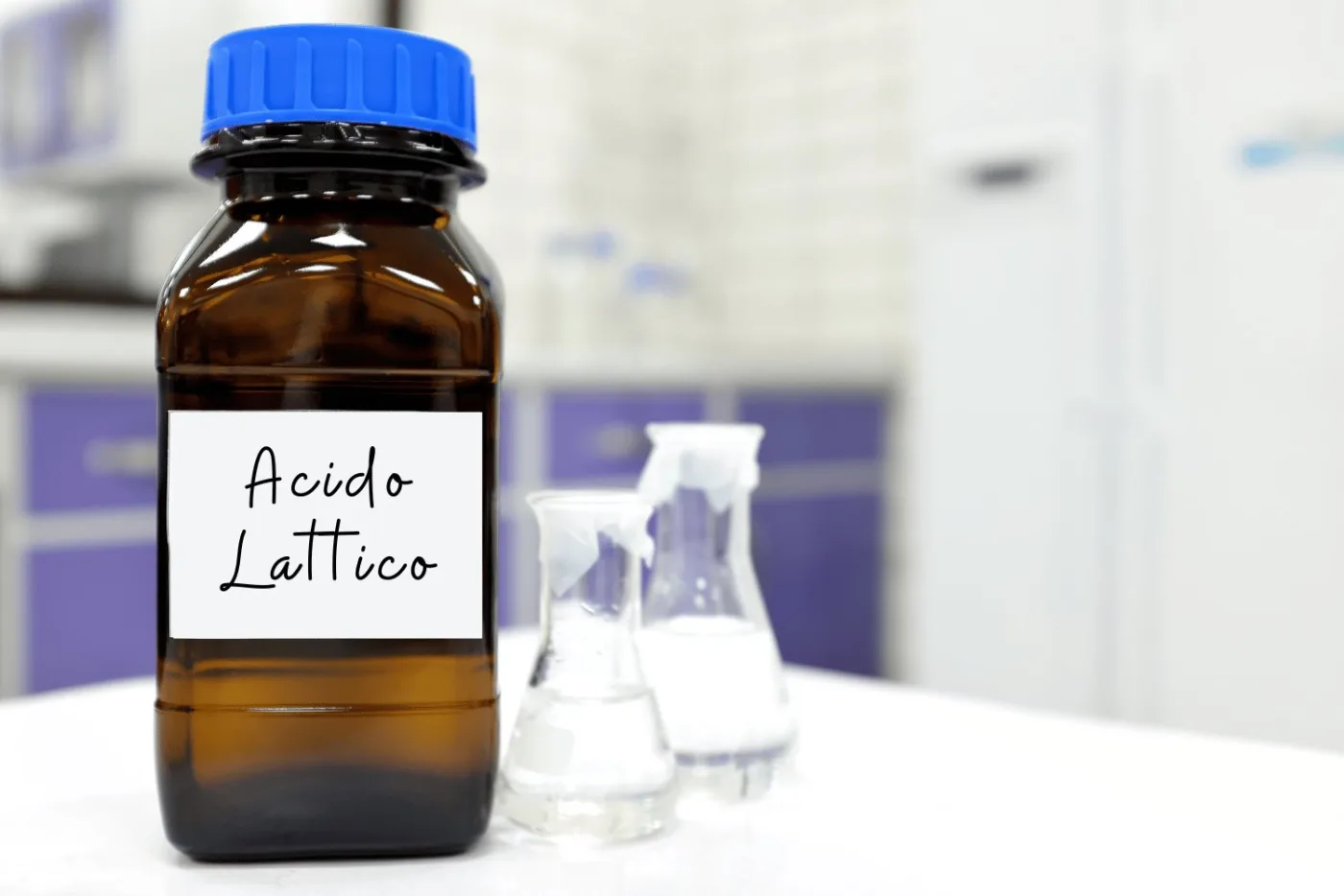 Bottiglia di vetro scuro con etichetta Acido Lattico e due beute da laboratorio sullo sfondo