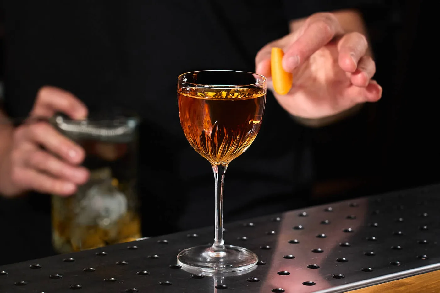 Hanky Panky ambrato in coppa Nick and Nora mentre il bartender spreme un twist di arancia