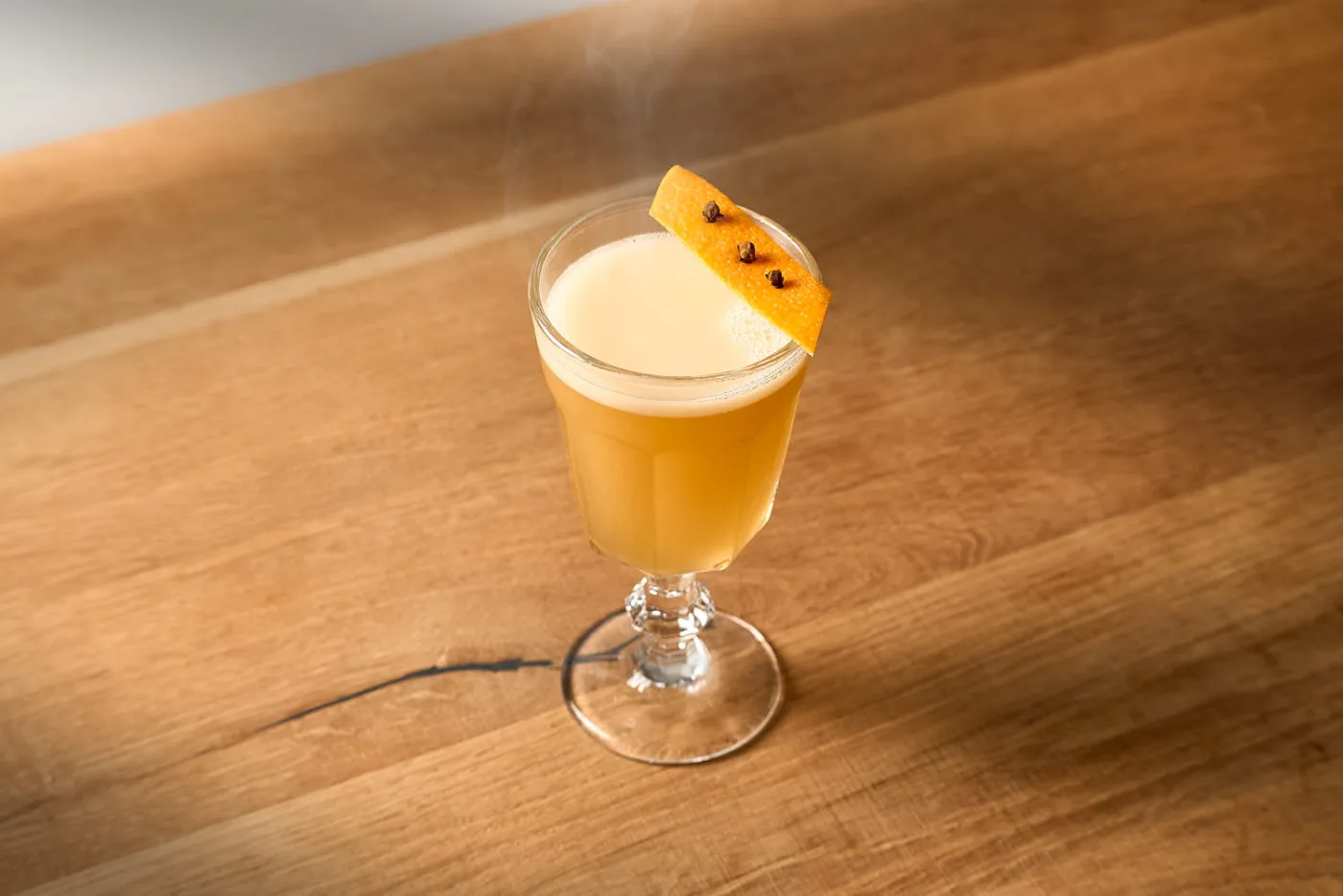 L'Hot Tiger Milk fumante servito in un bicchiere di vetro con stelo, decorato con una scorza d'arancia e tre chiodi di garofano