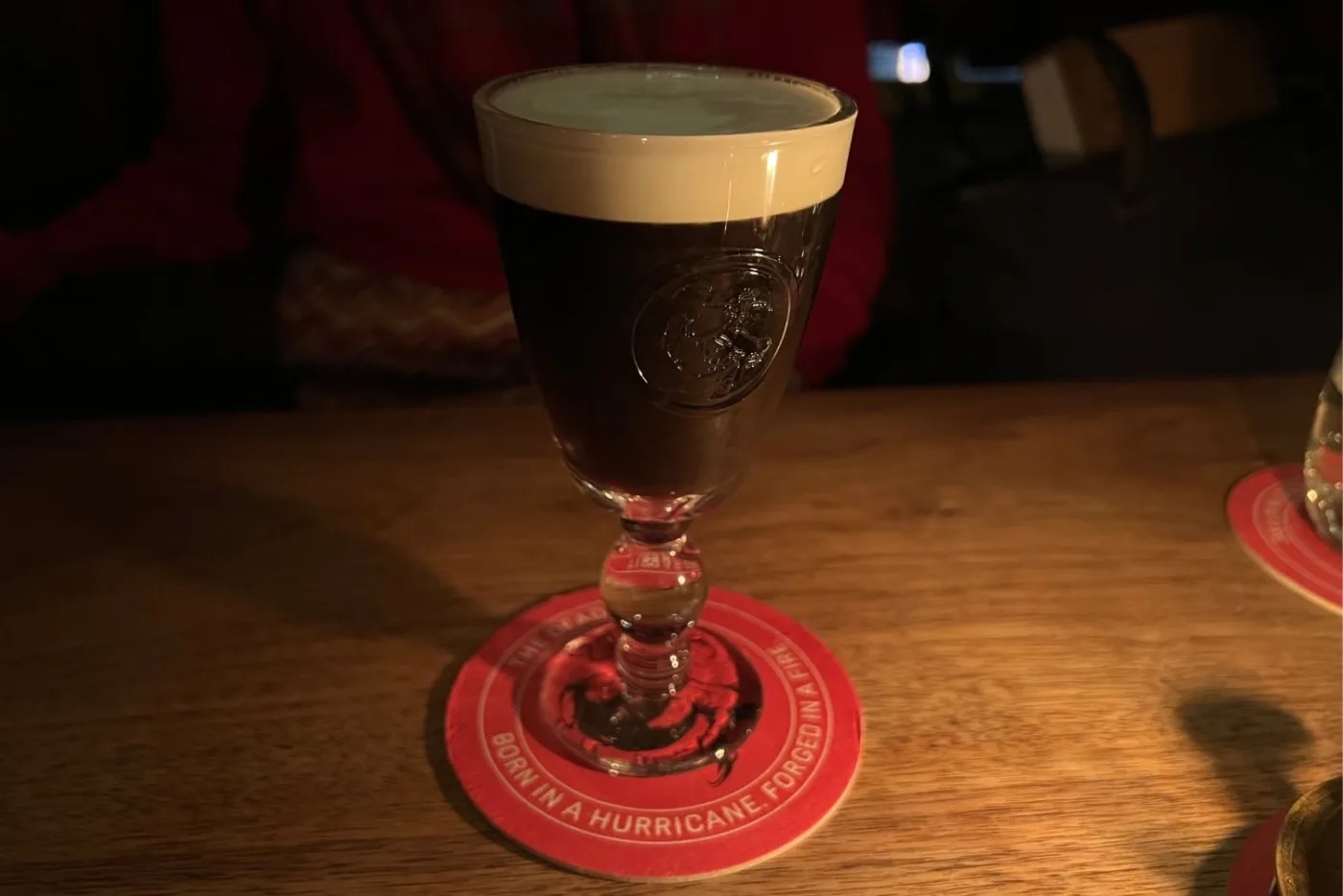 Un Irish Coffee con lo strato di panna in superficie servito nel calice del Dead Rabbit di New York, su un sottobicchiere rosso