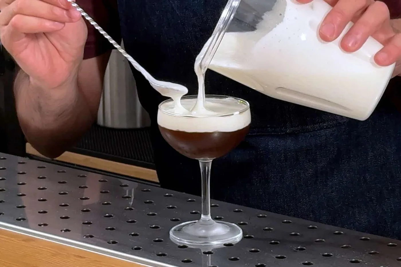 Su un banco bar una coppetta con un cocktail al caffè sul quale viene versata una foam al kefir dal contenitore di un milkshake mixer