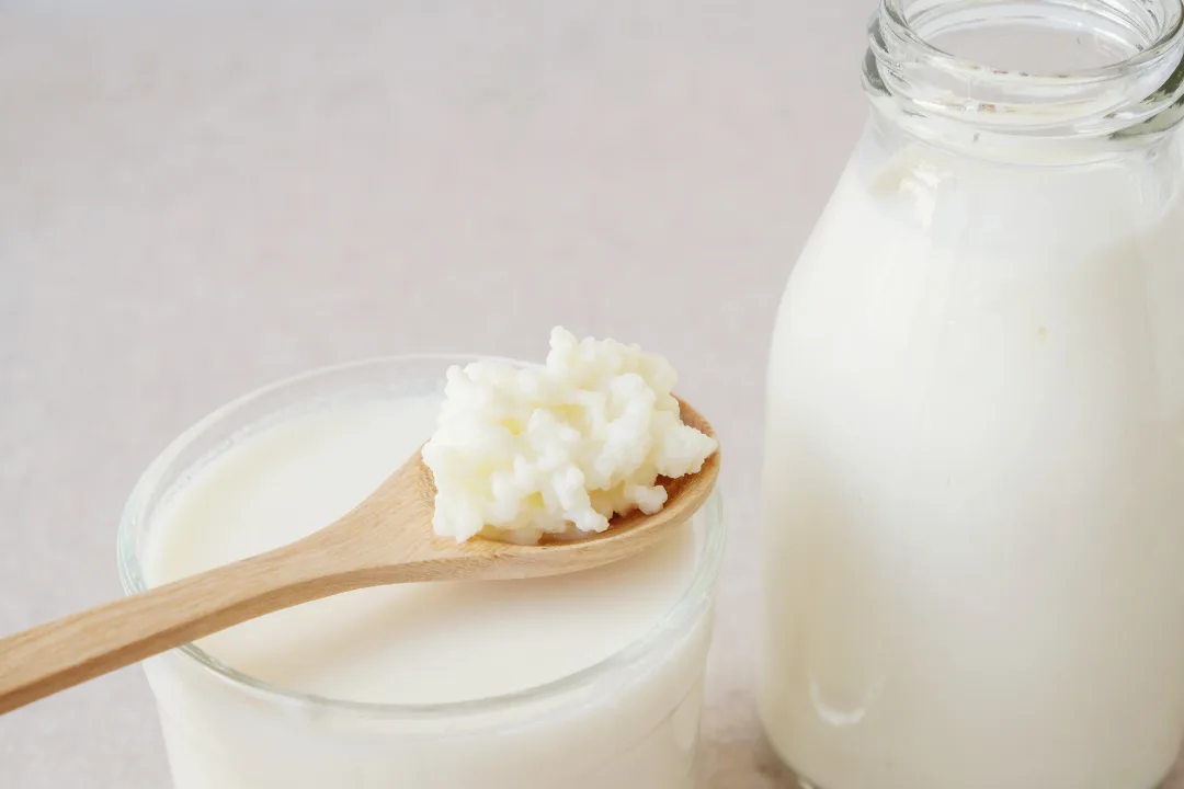 Grani di kefir di latte su un cucchiaio di legno, sopra un bicchiere di kefir e accanto a una bottiglia di latte