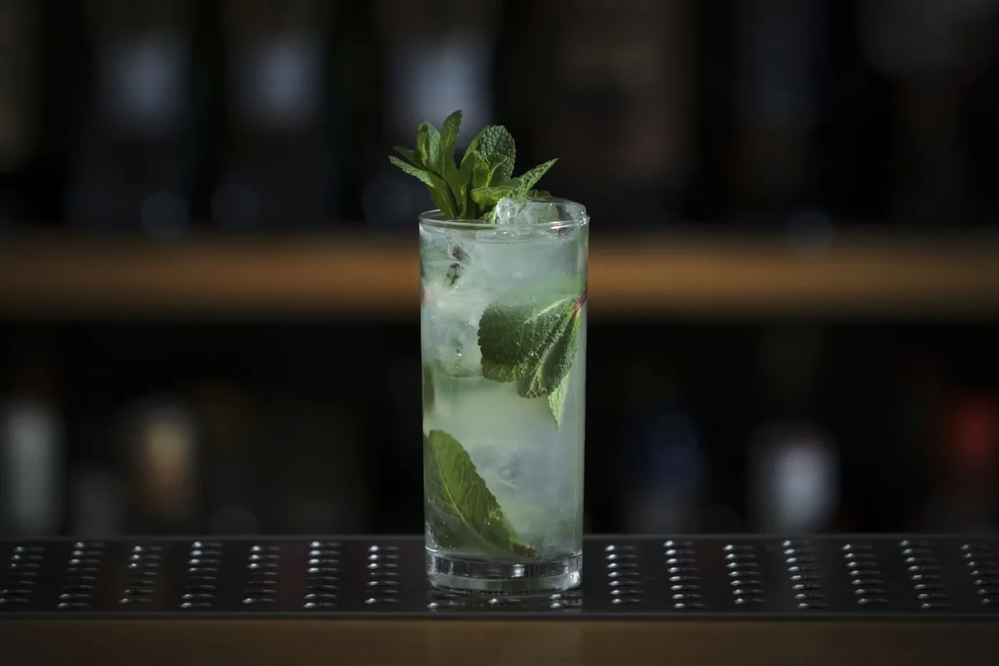 Mojito in tumbler alto con ghiaccio, foglie di menta fresca e ciuffo di menta come decorazione su banco bar