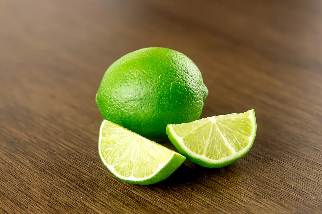 Lime intero e due spicchi tagliati su un tavolo di legno scuro