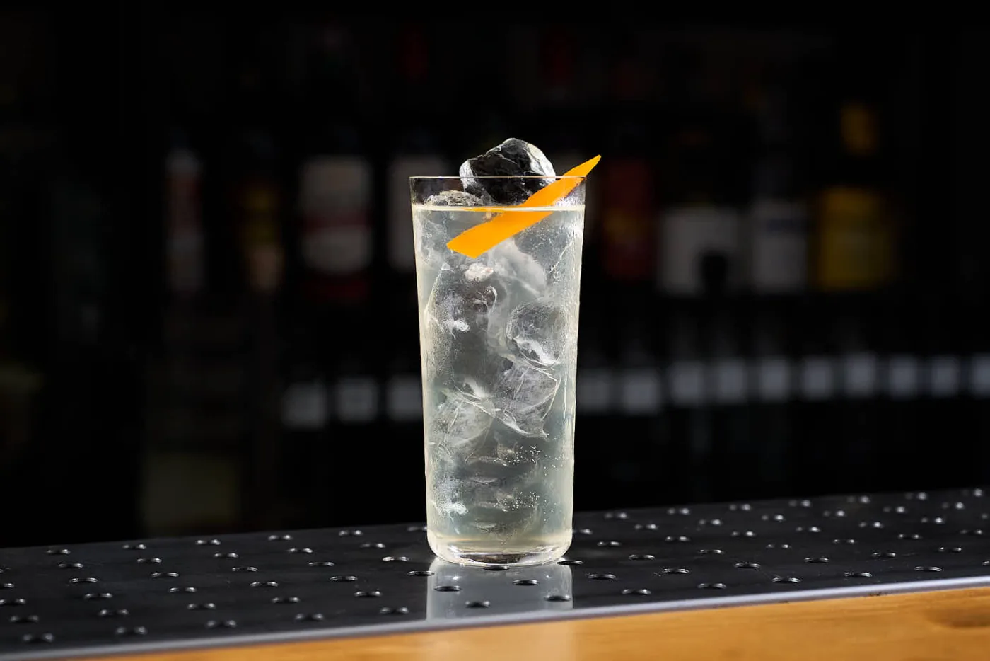 Long drink limpido con ghiaccio a cubetti e fettina di zucca su banco bar scuro