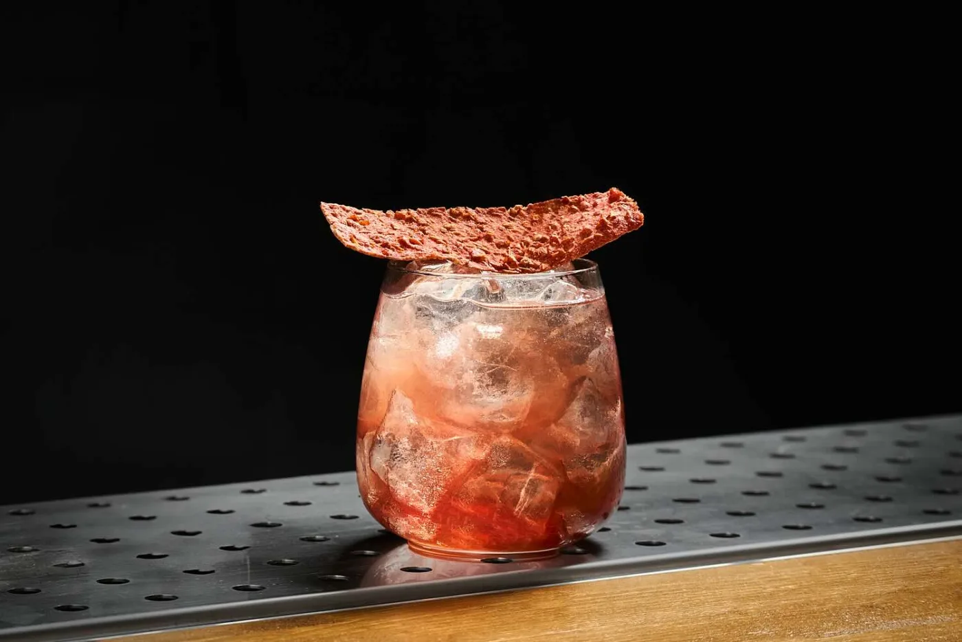 Mood Mediterraneo: long drink rosato su ghiaccio in tumbler tondeggiante decorato con cracker di pomodoro
