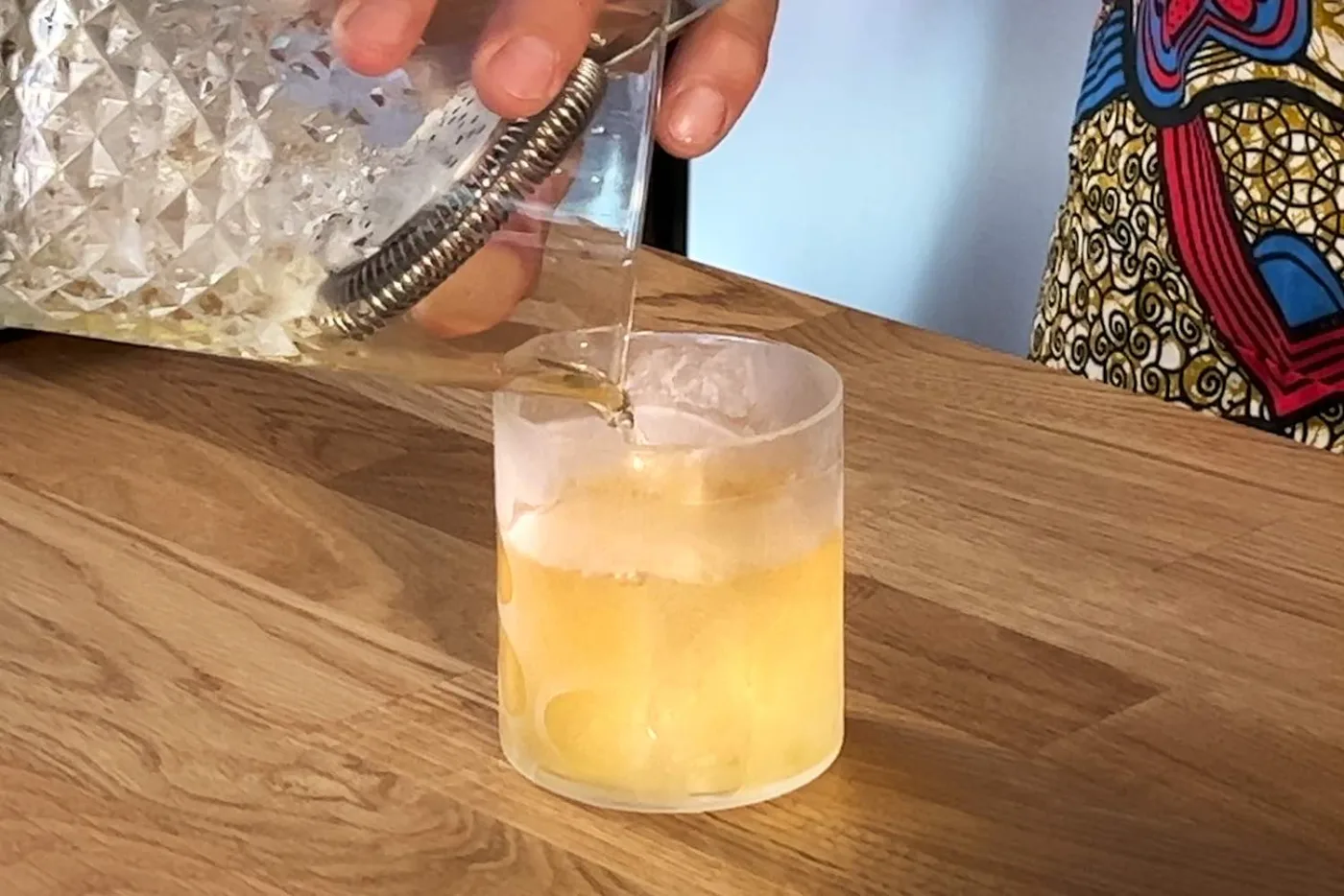 Il Negroni Bianco versato dal mixing glass in un tumbler basso smerigliato con ghiaccio, dal colore giallo chiaro