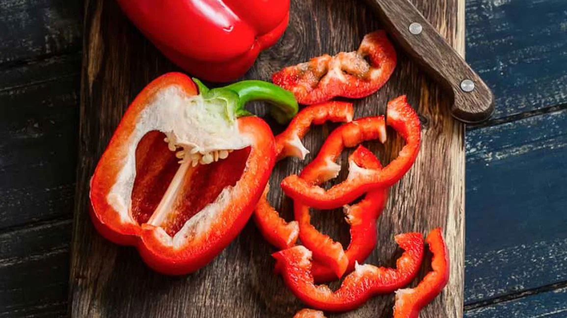 Peperone rosso tagliato a fette su un tagliere di legno con coltello