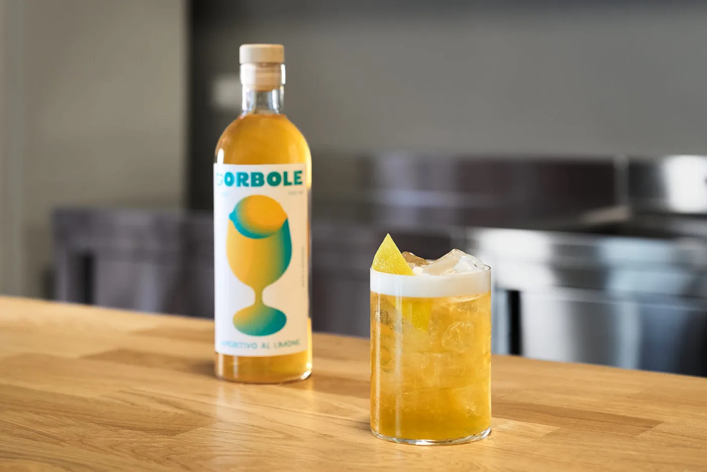 Radlerino in tumbler con ghiaccio, schiuma di birra e scorza di limone accanto alla bottiglia di Sorbole