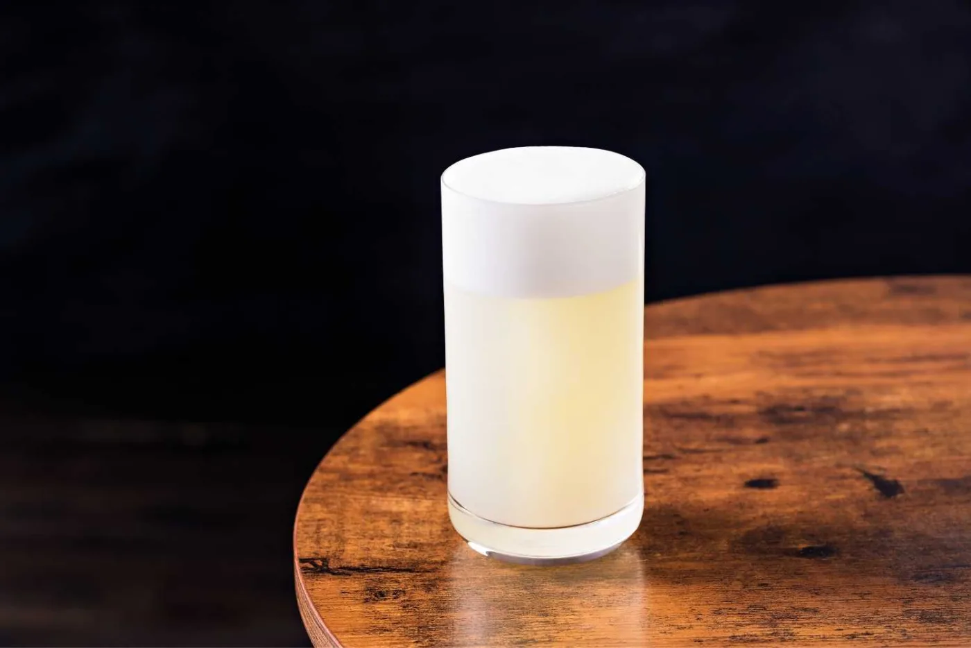 Ramos Gin Fizz in tumbler alto con cappello di schiuma bianca compatta su tavolino di legno