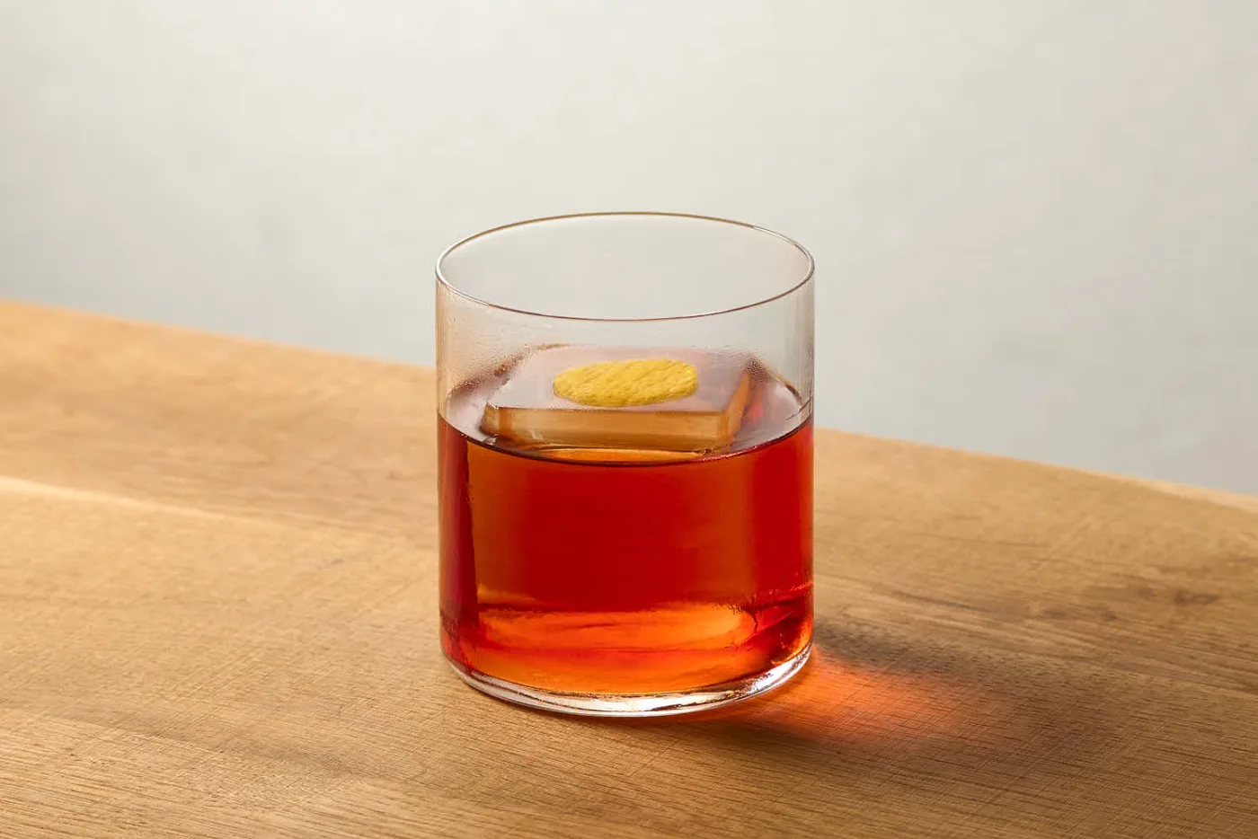 Negroni servito in tumbler basso con un cubo unico di ghiaccio e un disco di scorza di agrume