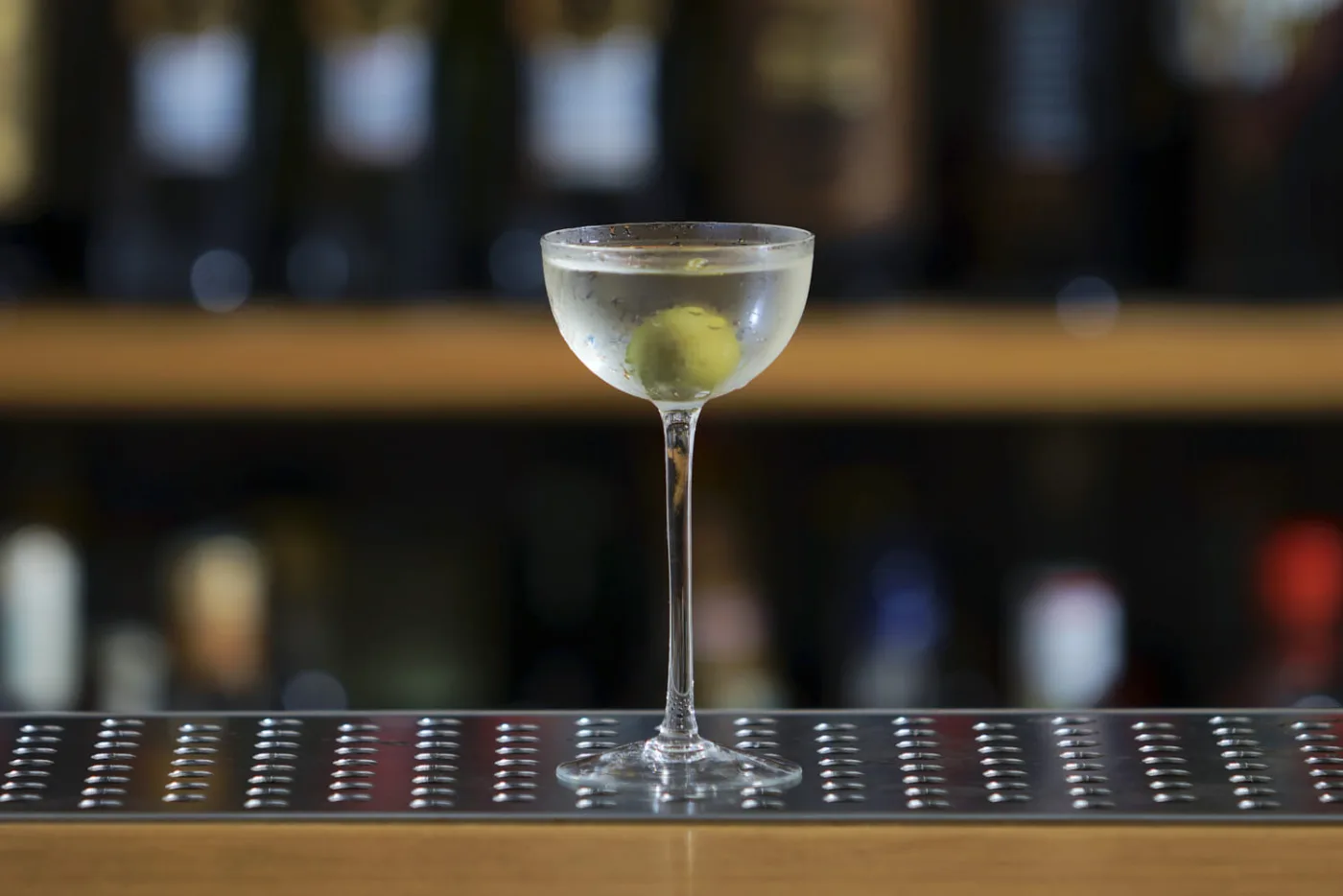 Cocktail Martini in coppetta ben fredda con oliva verde su banco bar in acciaio