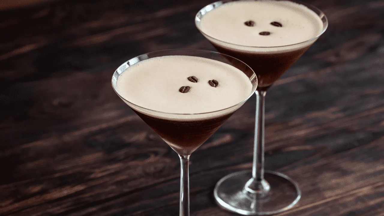 Due Espresso Martini in coppa Martini con schiuma compatta e tre chicchi di caffè su tavolo di legno scuro
