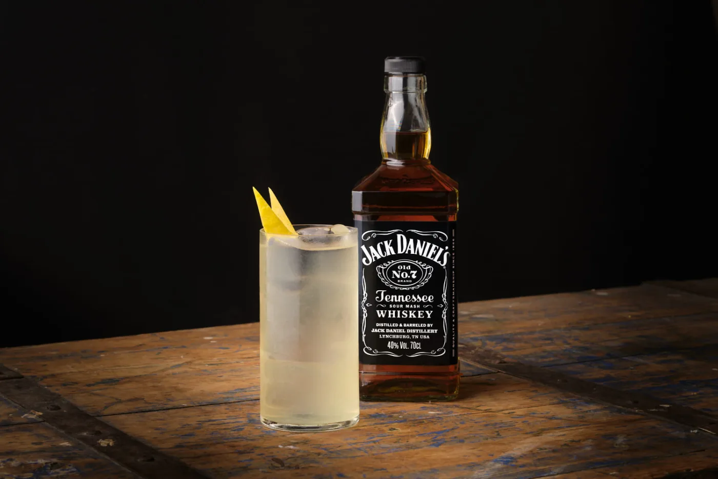 Lynchburg Lemonade in tumbler alto con ghiaccio e scorze di limone accanto a una bottiglia di Jack Daniel's Old No. 7