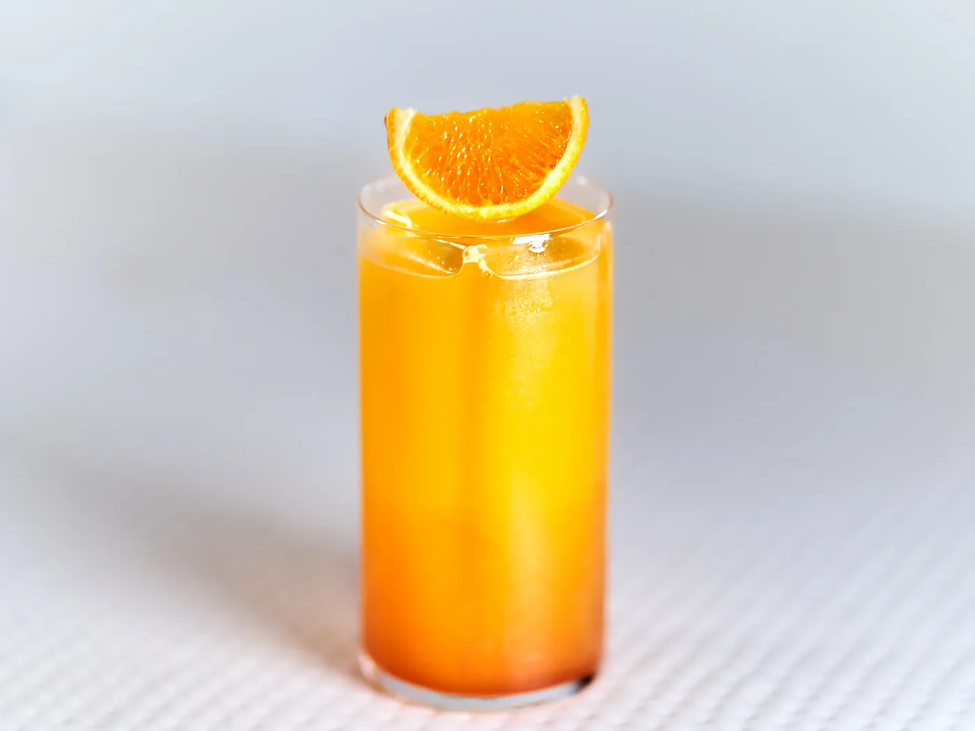 Il Tequila Sunrise servito in un tumbler alto con spicchio d'arancia, con la sfumatura dall'arancione al rosso della granatina sul fondo