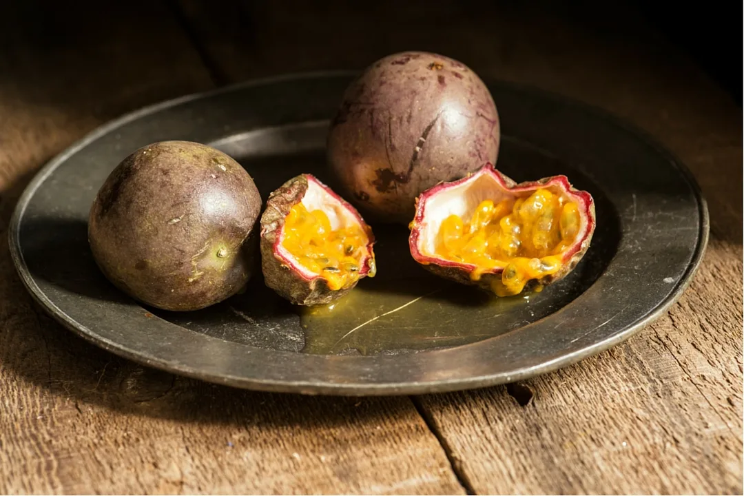 Frutti della passione viola interi e aperti su un piatto di metallo