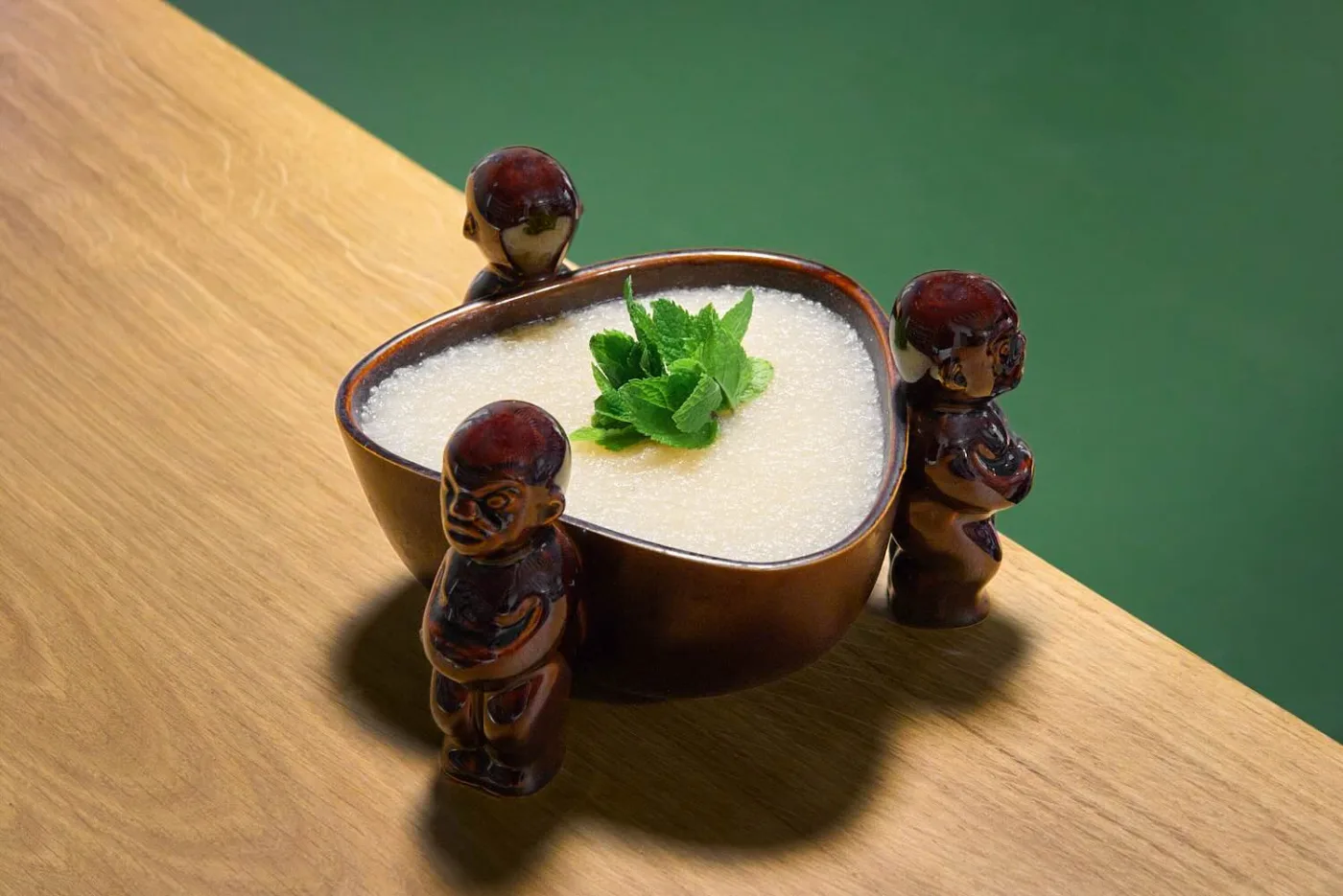 Lo Scorpion servito in una Scorpion Bowl in ceramica sorretta da tre figure tiki, con un ciuffo di menta al centro