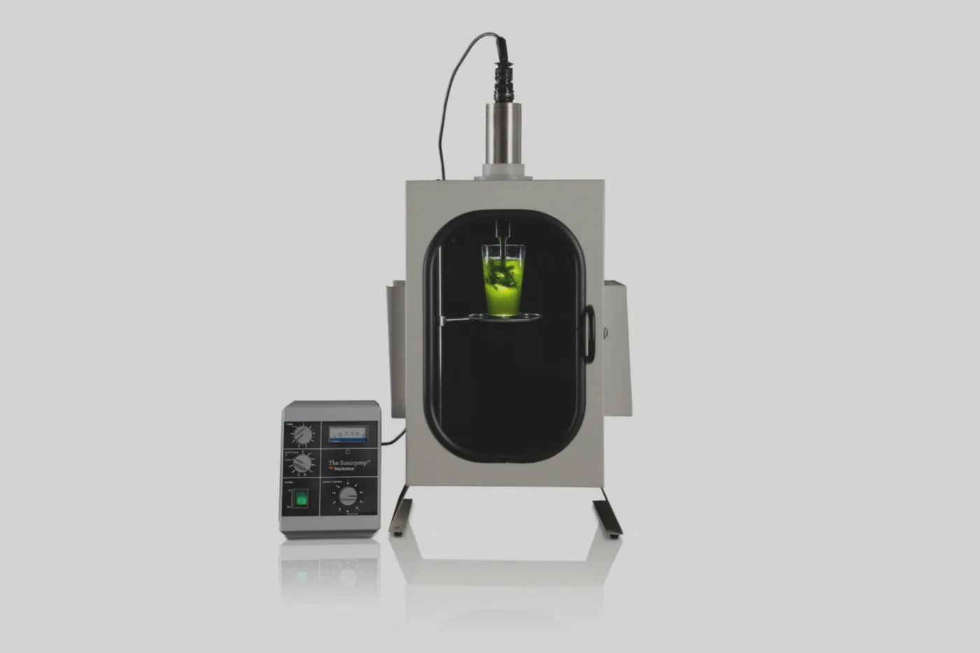 Sonicatore da laboratorio con camera stagna aperta e un bicchiere di liquido verde sotto la sonda, accanto al generatore