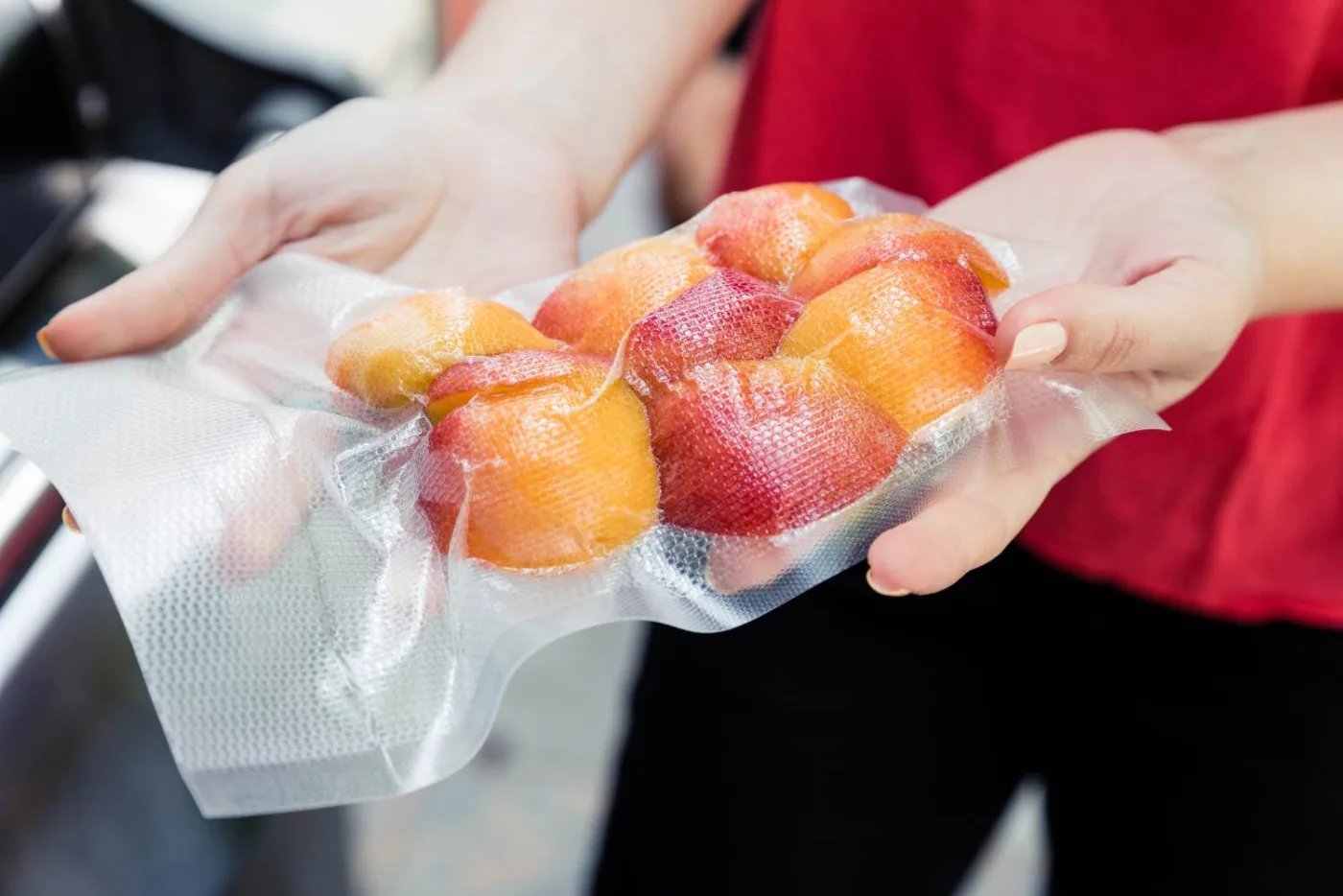 Sacchetto sottovuoto trasparente con pesche intere, tenuto in mano davanti alla macchina del sottovuoto