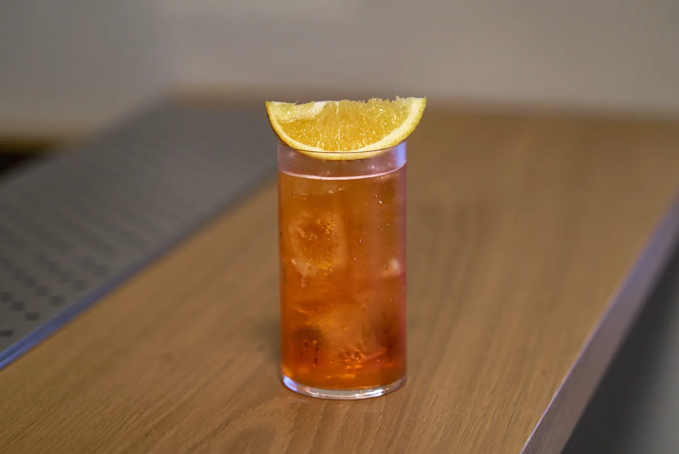Spritz in tumbler alto con ghiaccio e fetta d'arancia su bancone di legno
