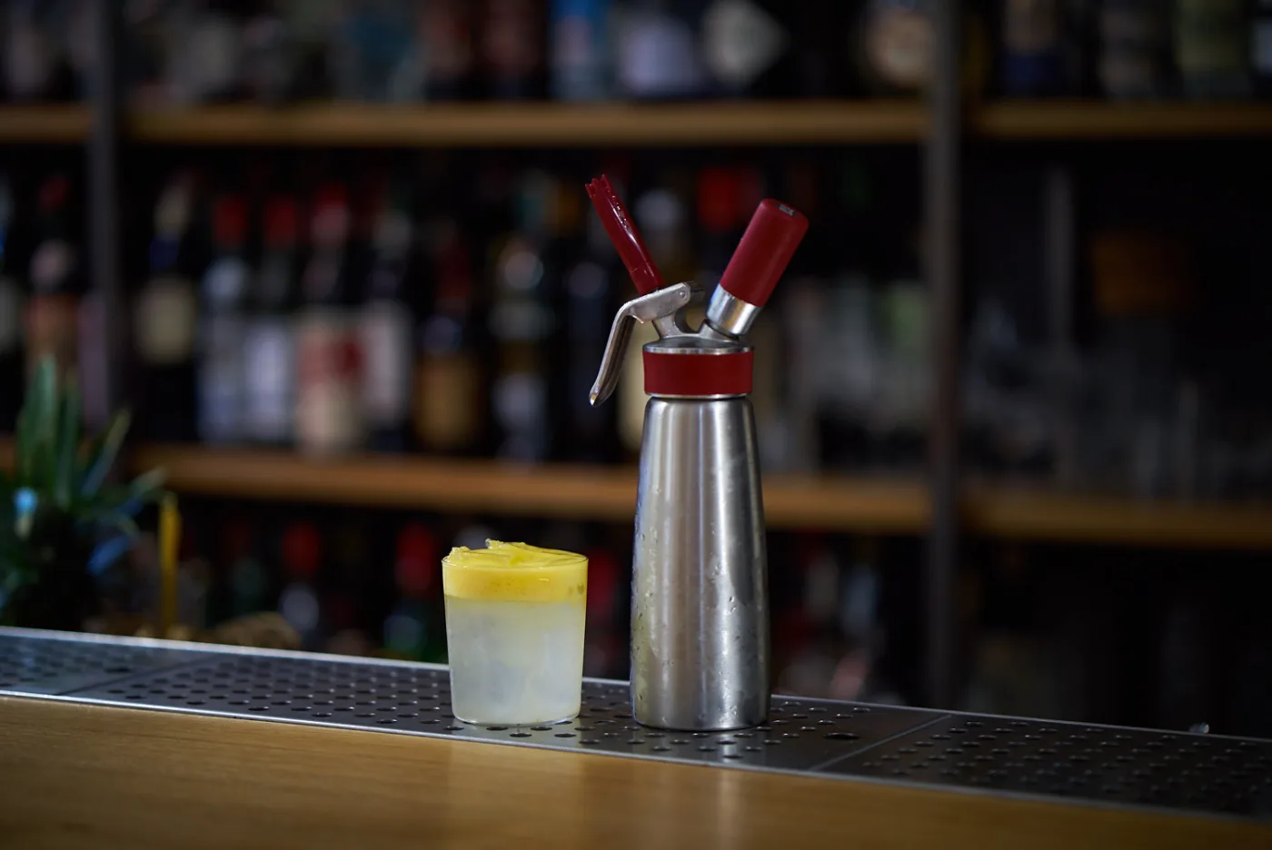 Drink con spuma di mango gialla accanto al sifone sul banco del bar