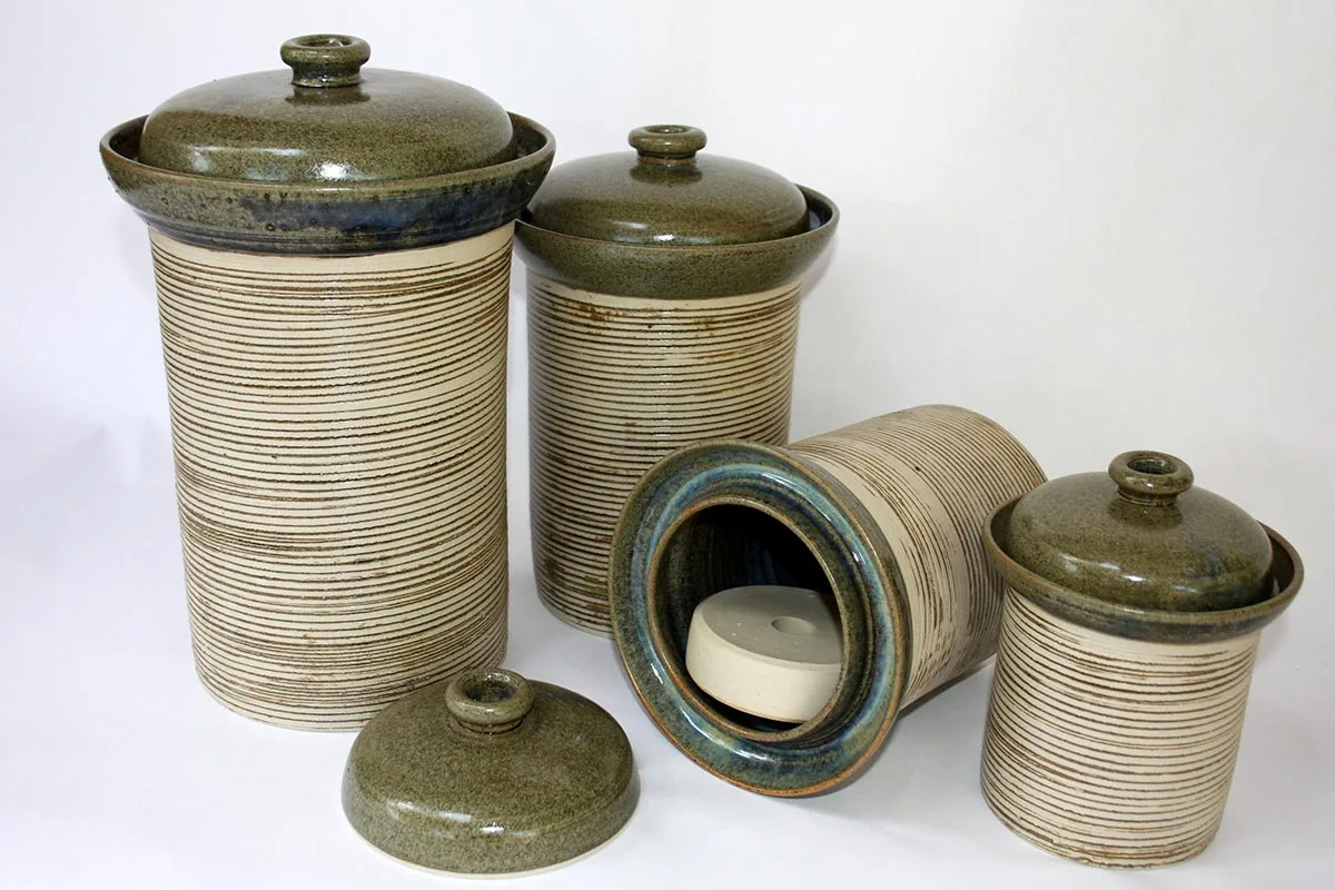 Quattro crock in ceramica per fermentazione, con coperchio e peso interno, uno aperto per mostrare il peso